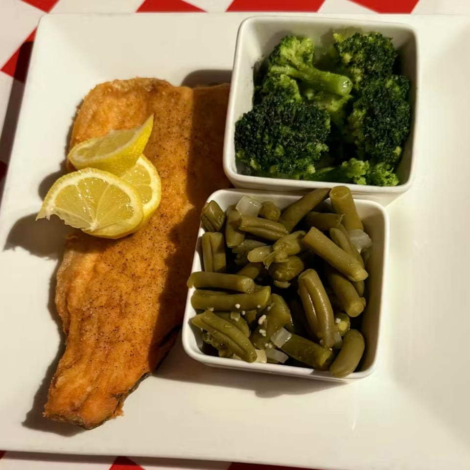 A plate of fried fish with lemon wedges, a side of green beans, and a side of broccoli.
