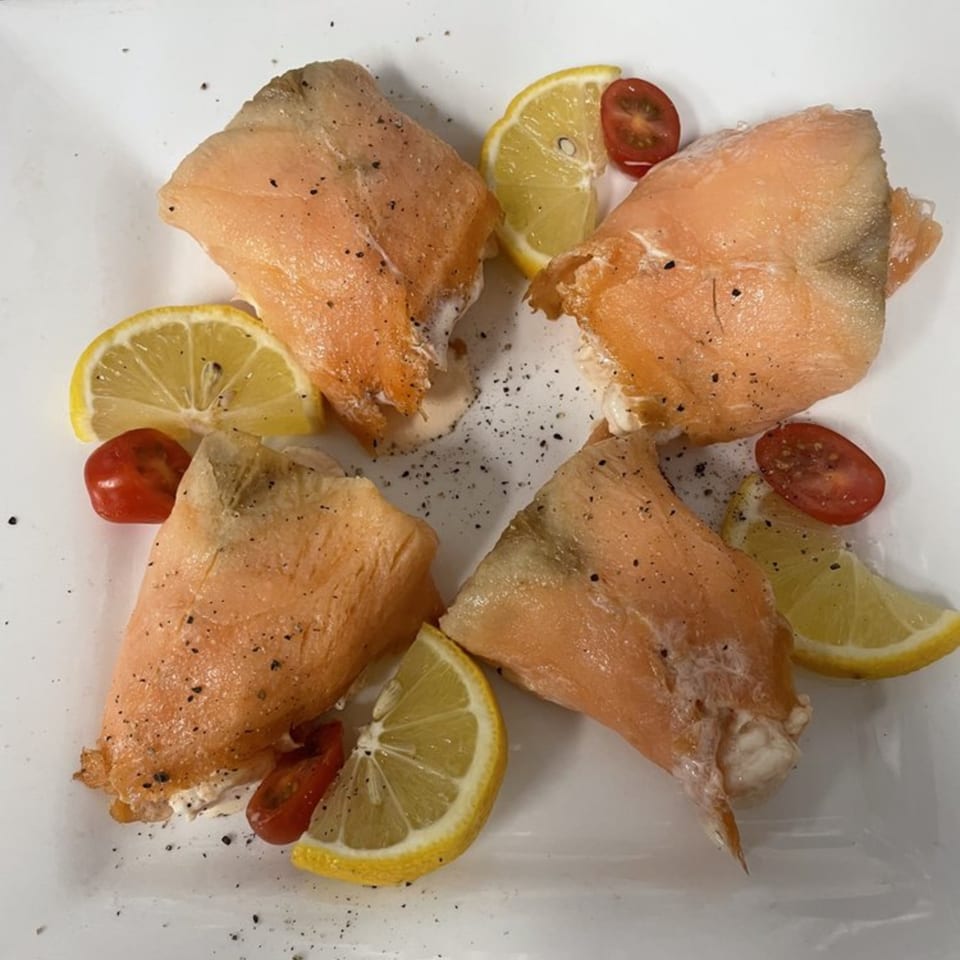 Four pieces of smoked salmon, garnished with lemon wedges and cherry tomato halves, on a white plate.